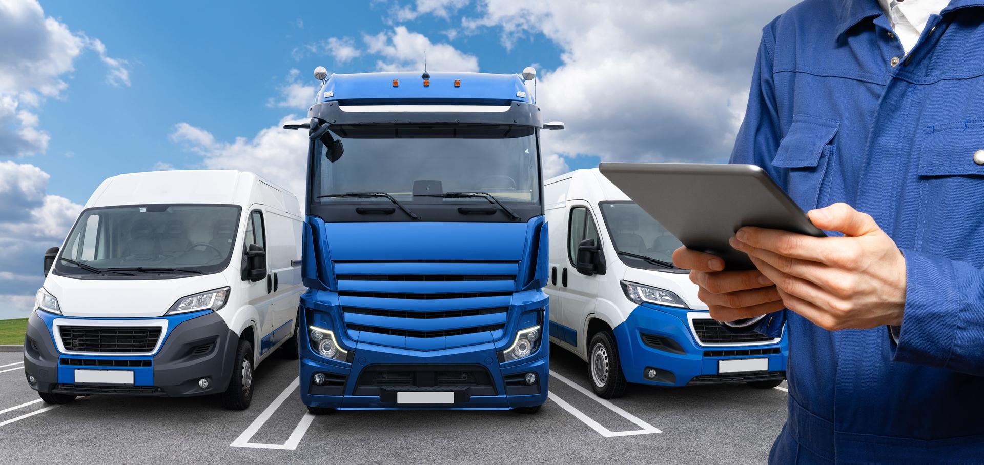 Manager with a digital tablet next to truck and vans.